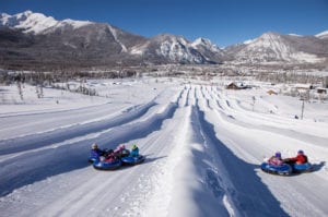 Two groups of tubers going down tubing hill at Frisco Adventure Park with mountain views